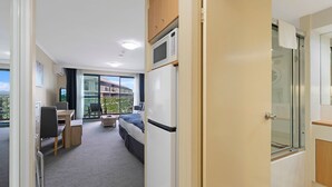 Une chambre d’hôtel comprenant un lit, un bureau, une chaise, une petite table, un four à micro-ondes, un réfrigérateur, une porte coulissante donnant sur un balcon et un espace douche.