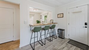 Una cocina con encimera de madera, tres taburetes de bar, un cubo de basura y una puerta con perchero.