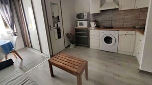 A compact kitchen with a microwave, kettle, and washing machine. There's a wooden bench in the center of the room. - Studio Cabin 4 Pers, Cap d'Agde, Near Beach (Cap d'Agde)