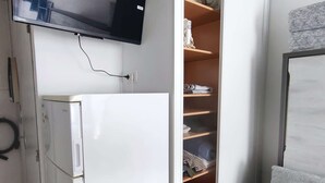 A compact room with a white refrigerator, a built-in shelf unit with folded clothes, and a mounted television. - Studio Cabin 4 Pers, Cap d'Agde, Near Beach (Cap d'Agde)
