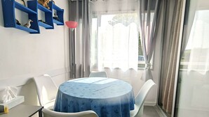 A dining area with a round table covered by a blue tablecloth, white chairs, and blue shelves on the wall. - Studio Cabin 4 Pers, Cap d'Agde, Near Beach (Cap d'Agde)