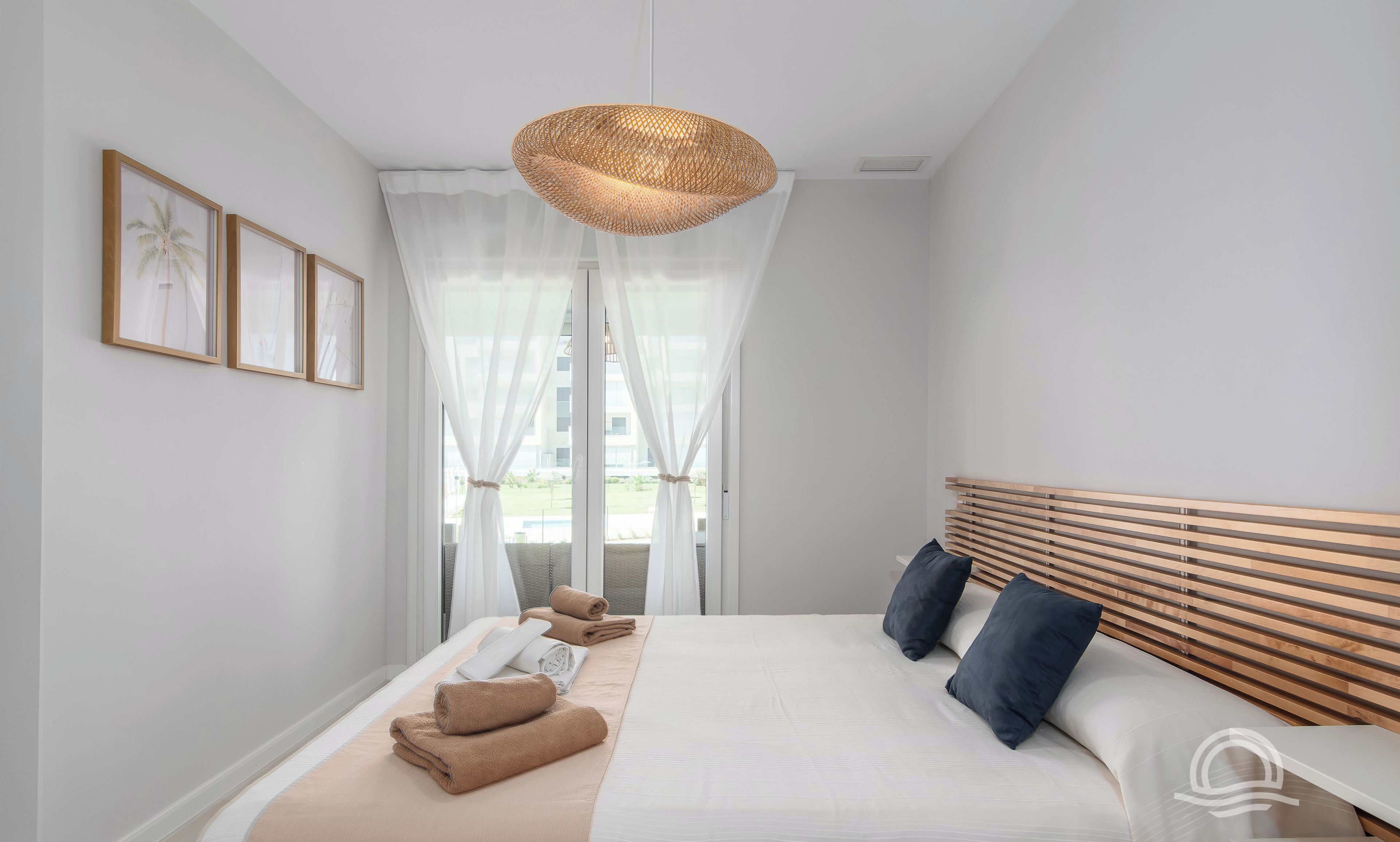 A modern bedroom with a large bed, a wooden headboard, and a large window with sheer curtains.