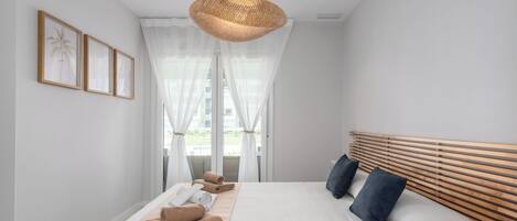 A modern bedroom with a large bed, a wooden headboard, and a large window with sheer curtains.
