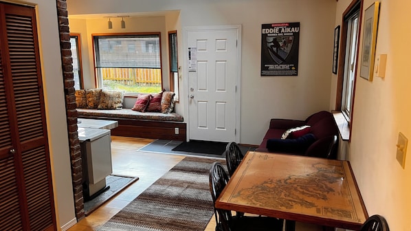 A cozy living area with a wooden table, a bench with cushions, a door, and a poster on the wall.