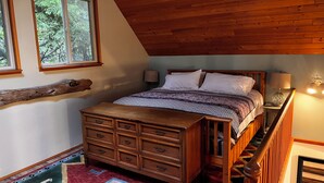 Una camera da letto con un letto in legno, una cassettiera, un comodino, una lampada e una scala.