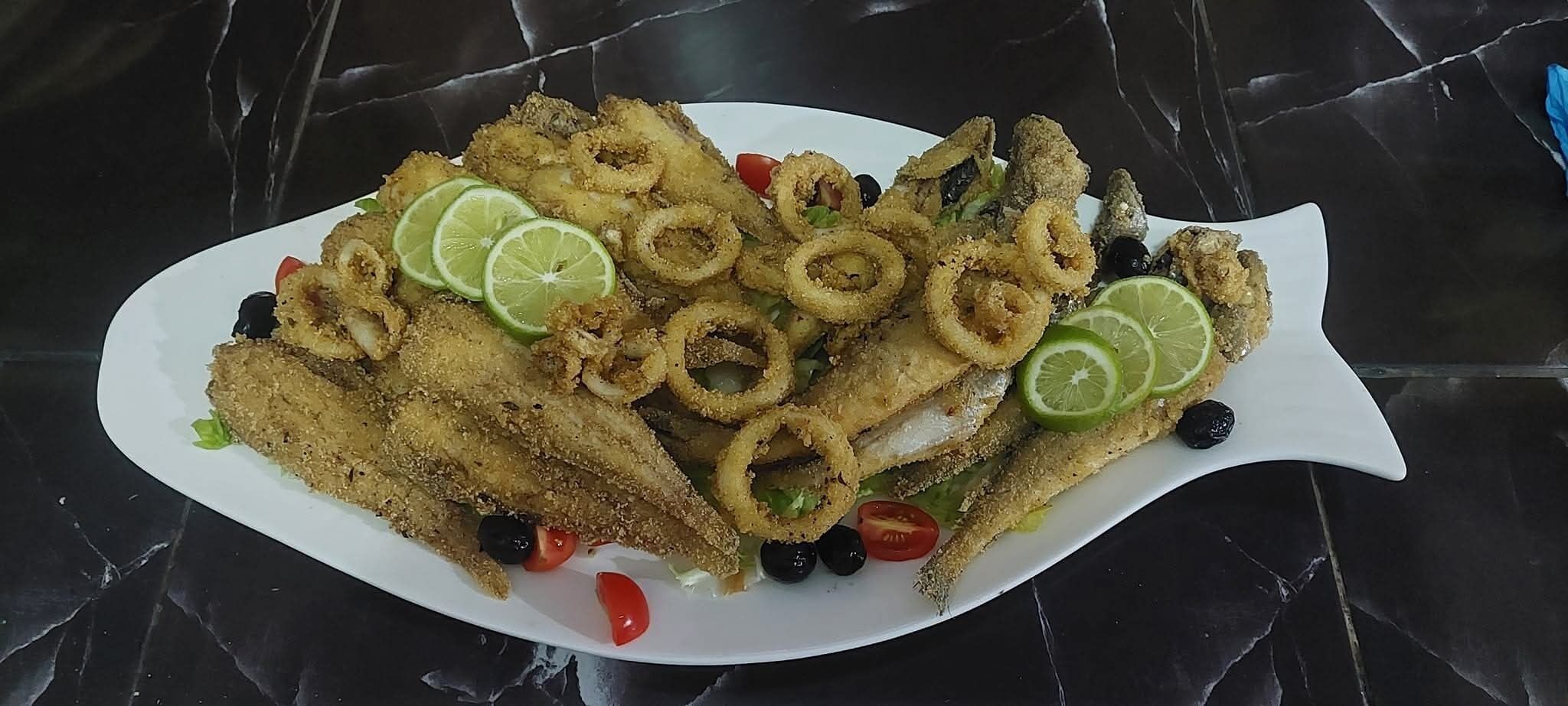 A plate of fried fish and calamari with lime slices and olives.