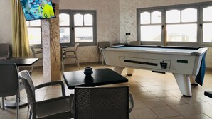 Une salle de billard équipée d’une table de billard, de chaises, d’un téléviseur et de grandes fenêtres.