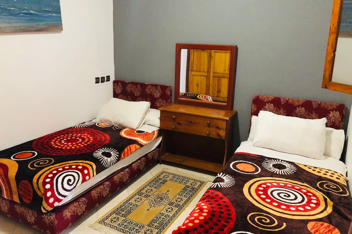 Una habitación con dos camas, un aparador de madera, un espejo y una alfombra estampada.