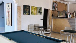 Une table de billard dans une pièce qui comprend un bar, des chaises et des œuvres d’art accrochées aux murs.