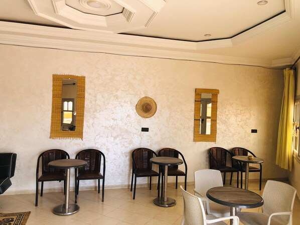 A room with a high ceiling, decorative molding, and a textured wall. There are several tables and chairs arranged for dining. - Hotel Marwa (El Ouatia)