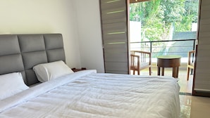 A neatly made bed with white linens in a room with a grey upholstered headboard.