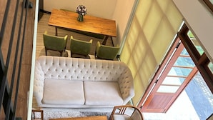 A modern living room with a sofa, a dining table with chairs, and a staircase.