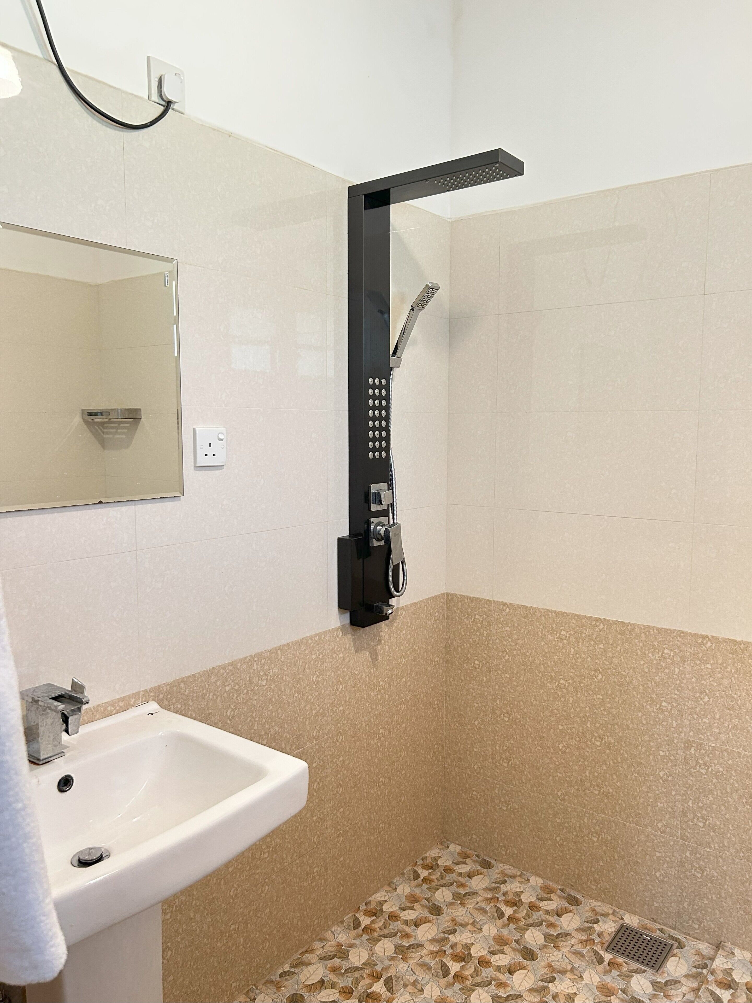 A bathroom with a white sink, a mirror, a shower with a control panel, and a patterned floor.