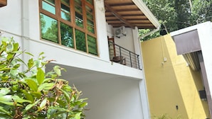 A two-story building with a balcony, a yellow wall, and a garden area with plants.