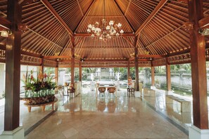 Amplio espacio interior con techo alto y una lámpara central, con una mesa y sillas de vidrio, y vistas a un jardín exterior.