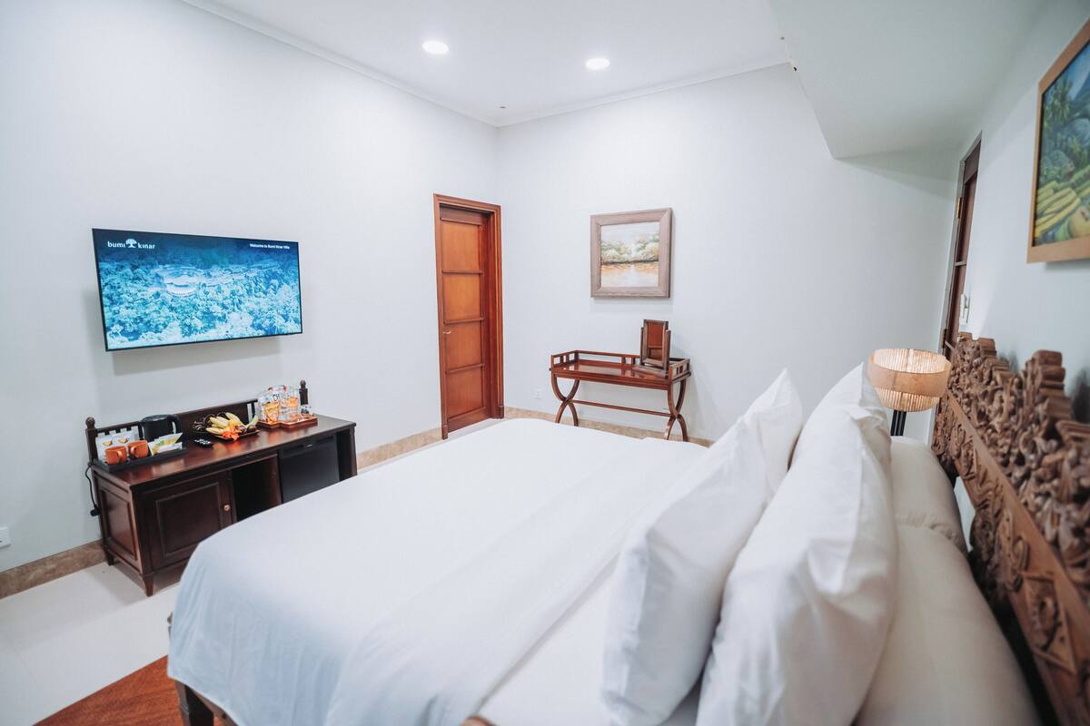 Un dormitorio con una cama, televisor montado en la pared, un escritorio de madera y una puerta.