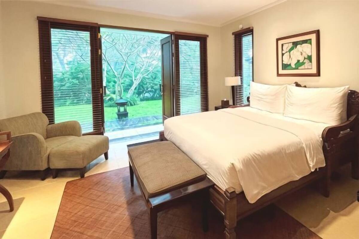 Un dormitorio con una cama, una silla, un banco y vistas a un jardín por una puerta corrediza.