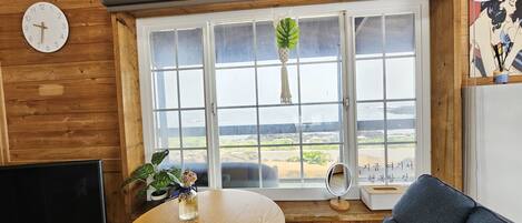 Un interior de madera con una mesa redonda de madera, un sofá gris, un televisor y una ventana con vistas al mar.