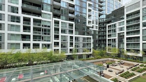 A modern multi-story building with a glass atrium and outdoor seating area. - Modern King West Condo | Central + Free Parking (Toronto)