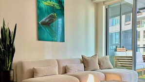 A modern living room with a beige sofa, a wooden coffee table, and a large window with a view of buildings. - Modern King West Condo | Central + Free Parking (Toronto)