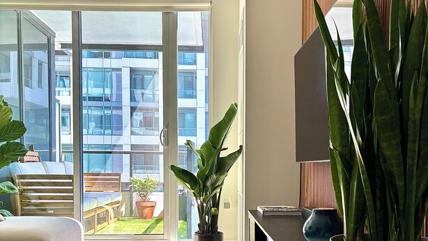 A modern living room with a large sliding glass door leading to a balcony, a wooden coffee table, a white sofa, and a potted plant. - Modern King West Condo | Central + Free Parking (Toronto)