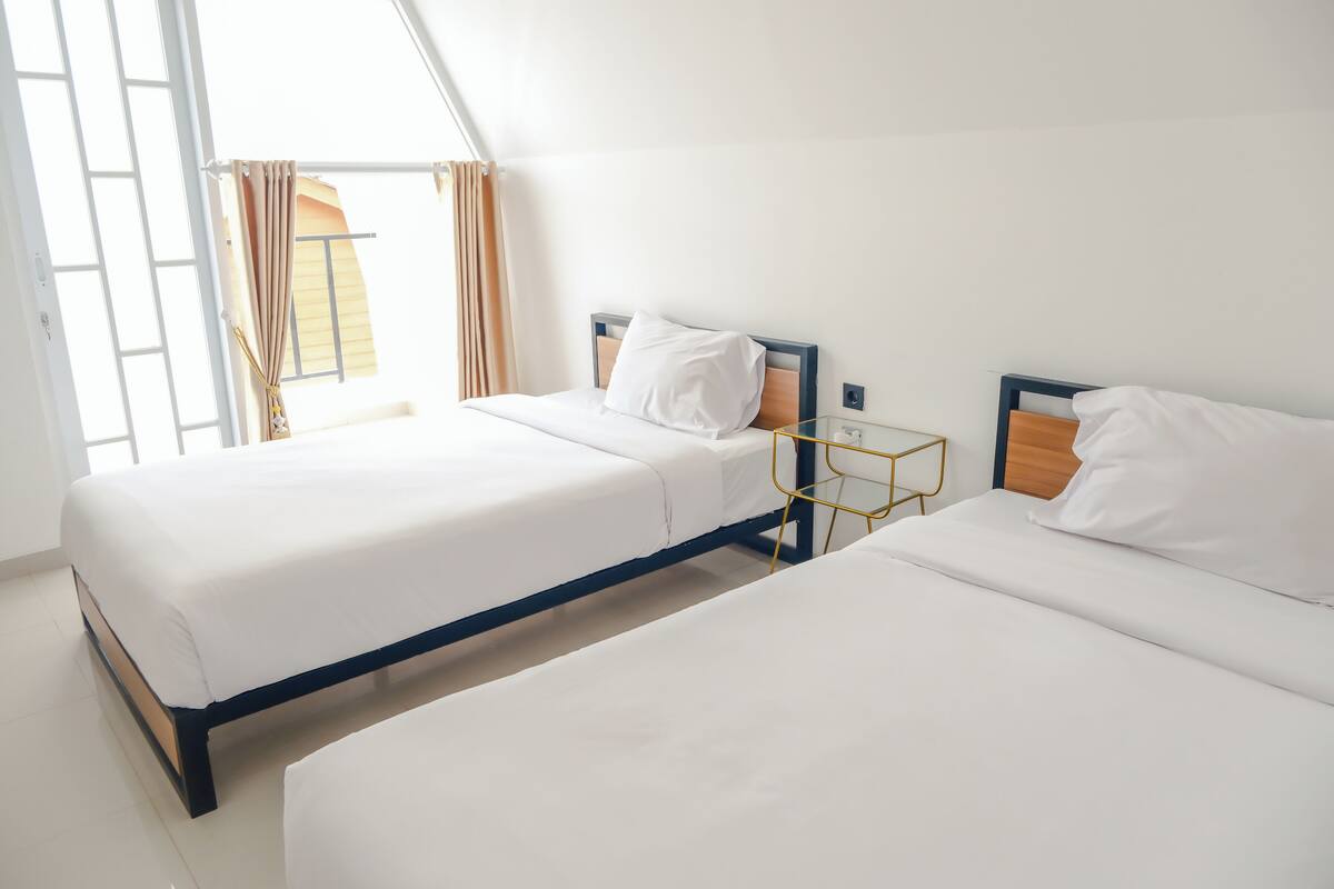Una habitación de hotel con dos camas, una mesita de noche y una ventana con cortinas.