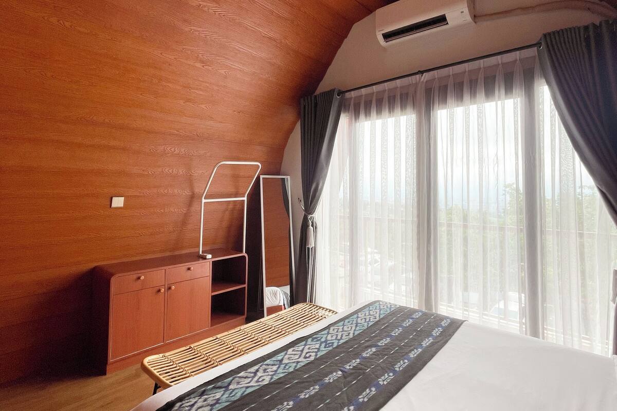 Un dormitorio con techo de madera, una cama con colcha estampada, un armario y una ventana con cortinas.