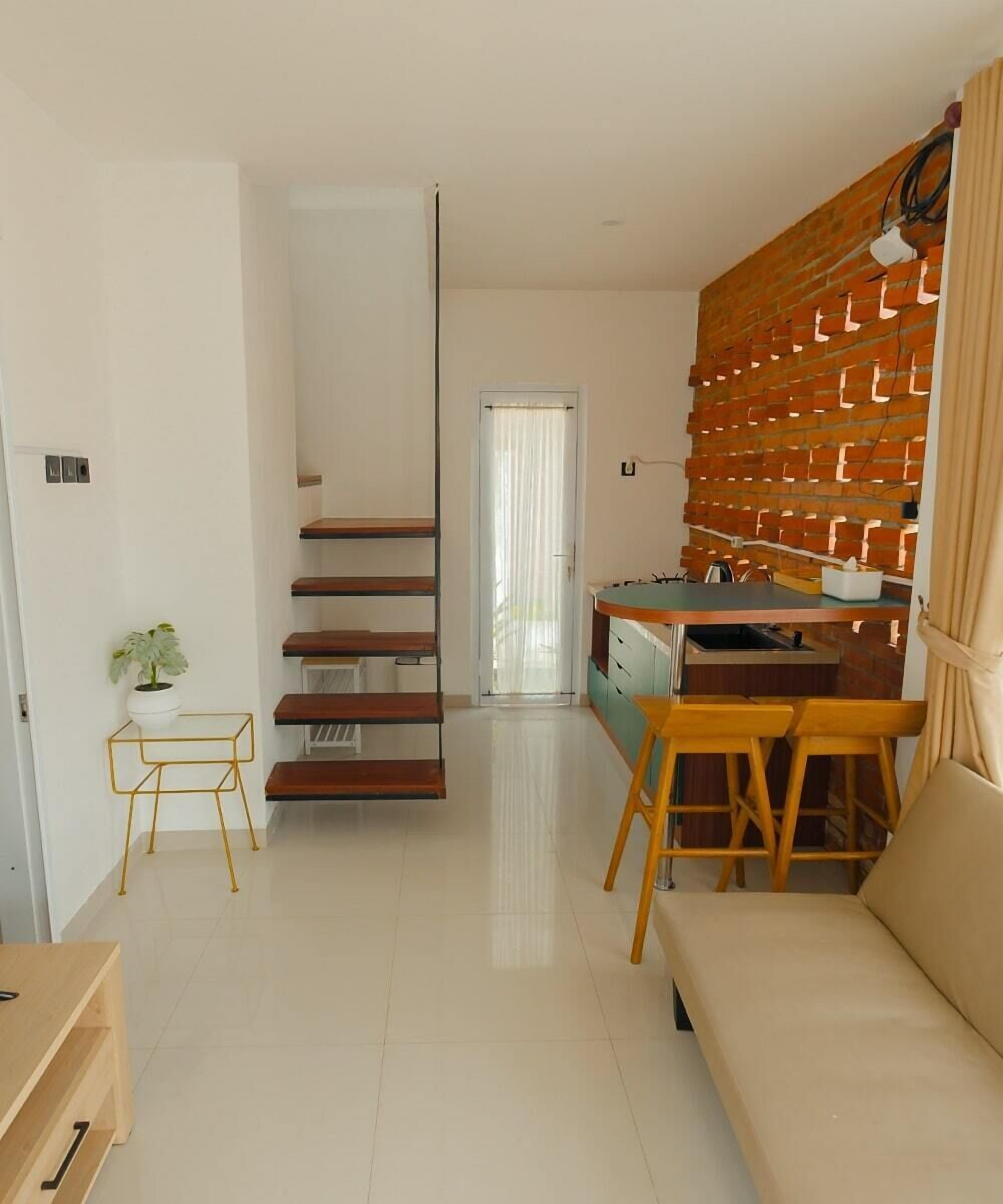 A modern living room with a staircase, a sofa, a dining area with a table and chairs, and a brick accent wall.