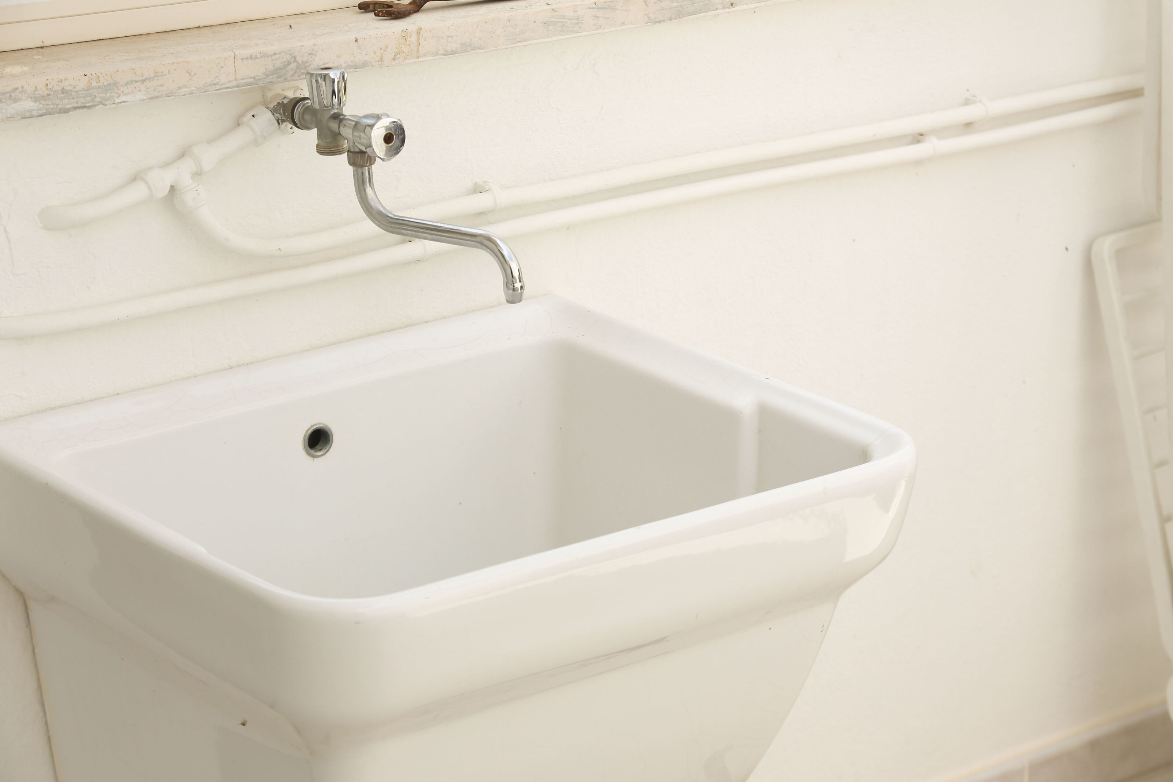 Un lavabo blanc dans une salle de bain, avec un robinet chromé et un tuyau blanc au-dessus.