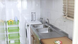 A compact kitchen with wooden cabinets, a stainless steel sink, a washing machine, and a brown stove.