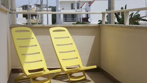 Two yellow rocking chairs on a balcony with a view of buildings and a railing.