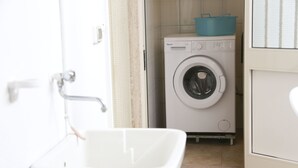 A small laundry area with a washing machine, a sink, and a door leading to another room.