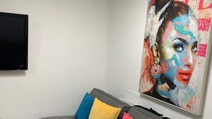 A modern living room with a grey sofa, colorful cushions, a flat-screen TV, and a vibrant magazine cover on the wall. - 5 Bed House - Sleeps 10 - Garden - Parking - Wifi (Aylesford)