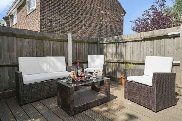 An outdoor patio with wicker furniture and a glass coffee table.