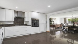 A modern kitchen with white cabinetry, a built-in oven, and a dining area with a table and chairs. - 5 Bed House - Sleeps 10 - Garden - Parking - Wifi (Aylesford)