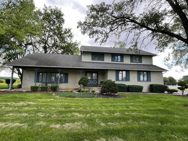 A two-story house with a brick facade, green shutters, and a covered porch. - Spacious 5-bed farmhouse w/Pool Table, Table Tennis Close to Columbus Zoo (Plain City)