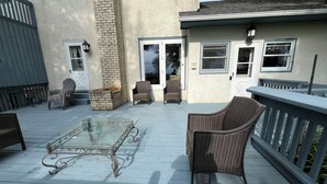 Une terrasse couverte, aménagée avec des meubles en osier, une table à plateau en verre et une porte dotée d’une fenêtre coulissante.