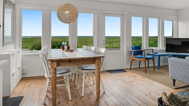 Una habitación amplia con una mesa de comedor de madera, sillas y un ventanal con vistas al mar.