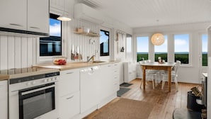 Una cocina moderna con armarios blancos, horno empotrado y comedor con mesa y sillas de madera.