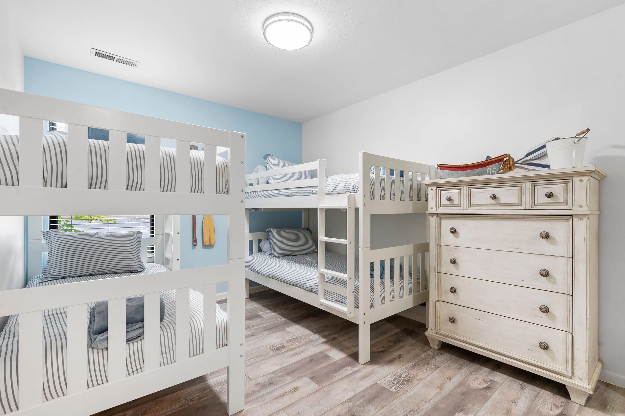 A room with bunk beds, a dresser, and a ceiling vent.