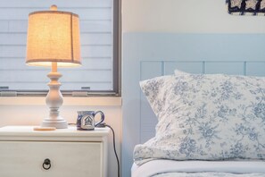 Una cama con ropa de cama estampada, una lámpara de noche y una taza sobre una mesita de noche.