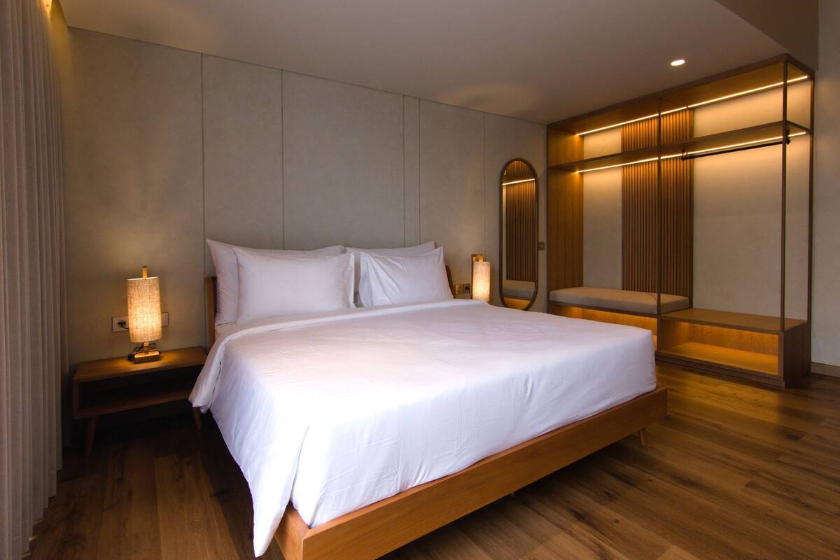 Ein großes Bett mit Holzrahmen, ein Nachttisch mit Lampe und eine integrierte Sitzbank mit Stauraum.
