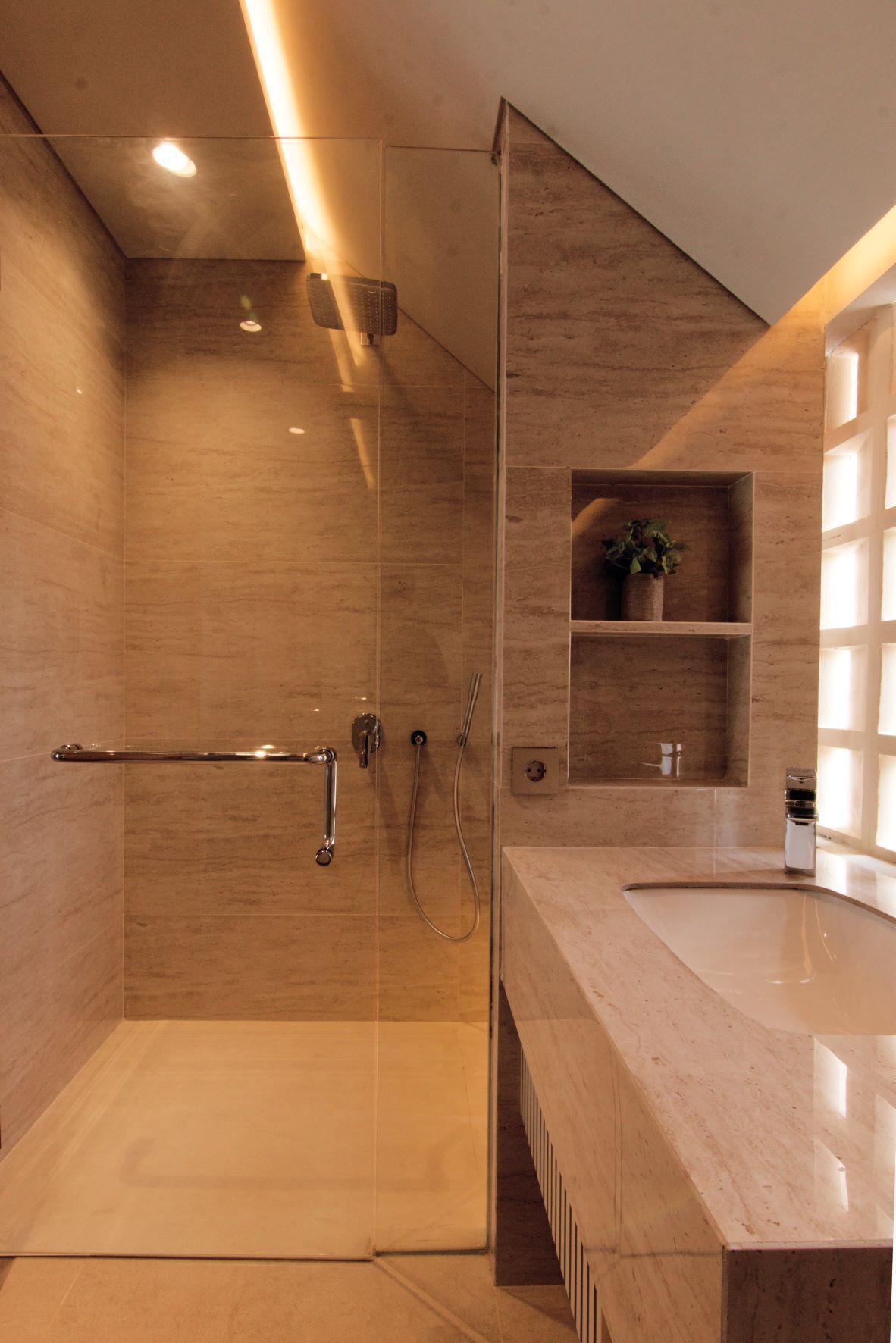 A modern bathroom with a glass shower enclosure, a marble countertop, and a built-in shelf with a plant.