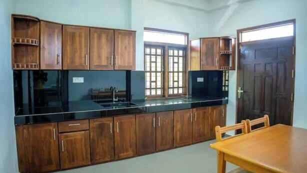 Una cocina con armarios de madera, encimera negra y una mesa de comedor.