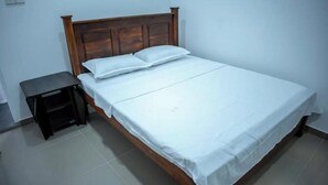 Una cama individual con cabecera de madera y ropa de cama blanca en una habitación con suelo de baldosas.