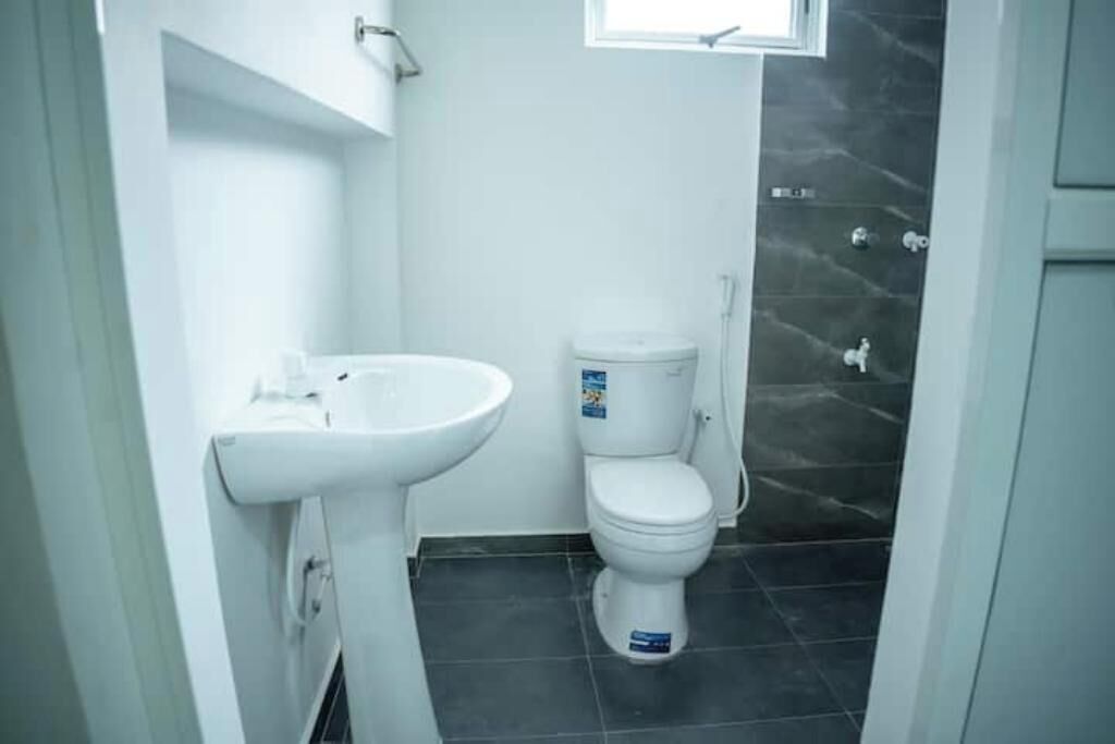 Un bagno con lavandino bianco, WC e zona doccia con piastrelle scure.