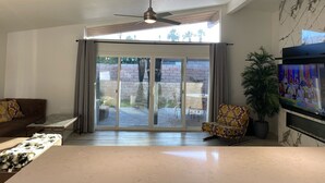 Un salon spacieux doté d’un ventilateur de plafond, d’un grand téléviseur et d’une porte-fenêtre coulissante donnant sur un espace extérieur.