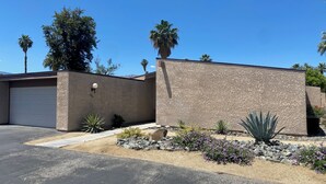 Un quartier résidentiel comprenant un garage, un mur recouvert d’enduit et un jardin aménagé avec des plantes typiques des régions désertiques.
