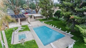 Une piscine rectangulaire entourée d’une terrasse, de chaises longues et d’un petit jacuzzi.