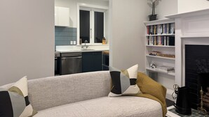 A modern living room with a sofa, a fireplace, a bookshelf, and a kitchen visible through an open door. - Discerning Accommodation in Thorndon (Wellington)